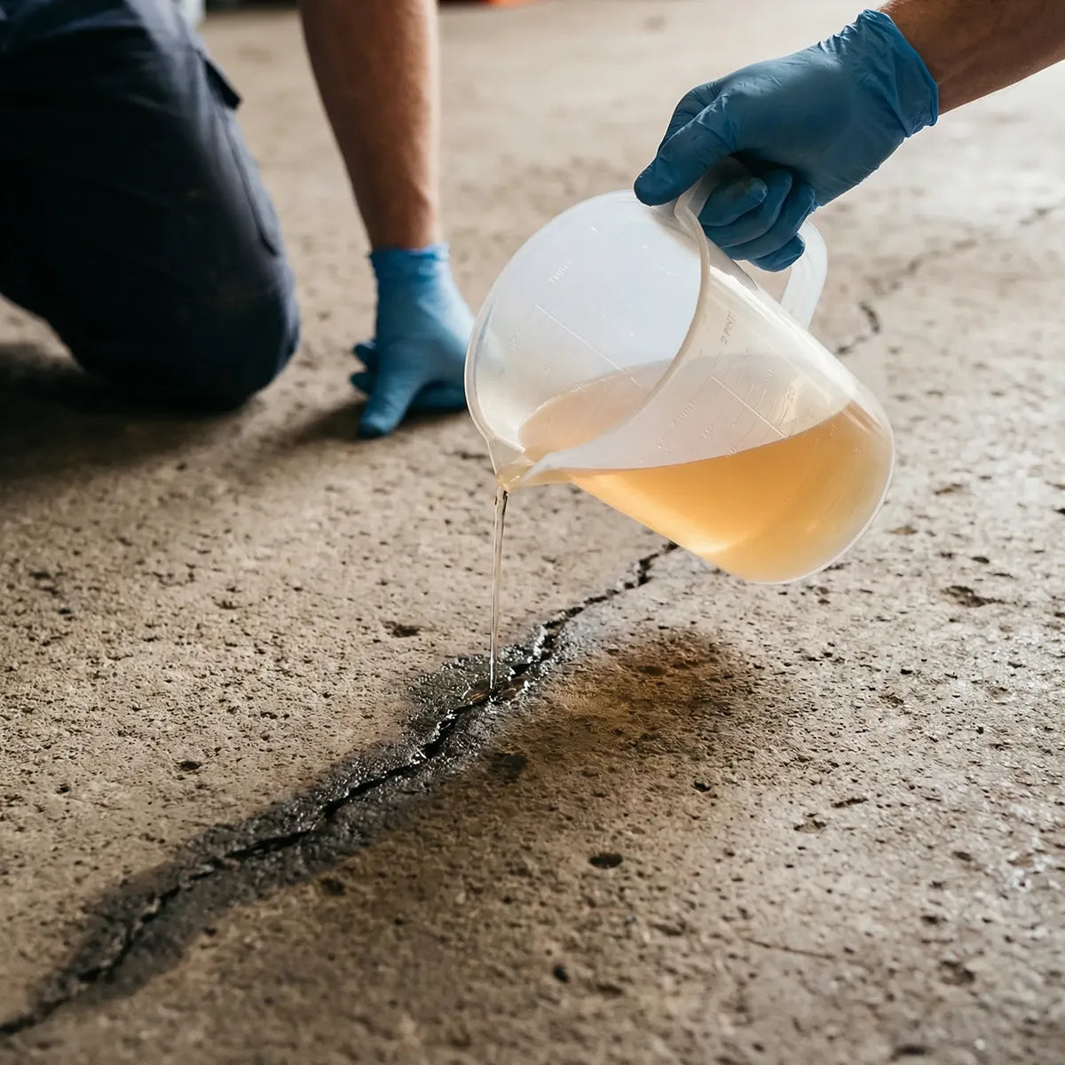 Person pouring a crack repair epoxy liquid into a crack on a concrete floor